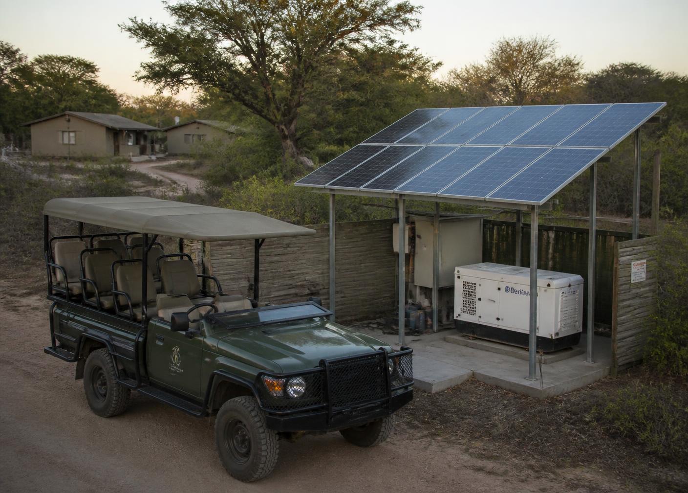 Game-drive vehicle beside a solar array and generator at a remote safari camp